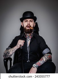 Brutal handsome man with tattooed body and cigar in his mouth sitting on chair