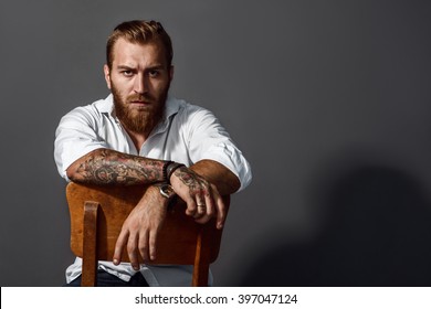 Brutal handsome man with tattooed body sitting on chair