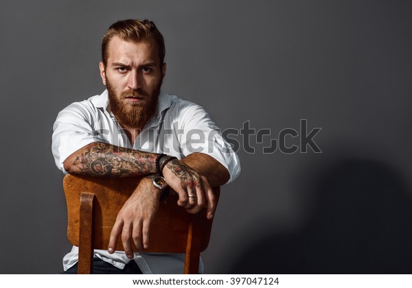 Brutal\
handsome man with tattooed body sitting on\
chair