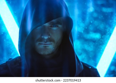 A brutal man with a brave look, dressed in a black robe with a hood on his head, stands in the light of neon lamps. Fantasy hero. Science fiction about space and the future world. Cyber theme.