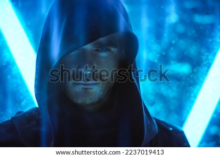 A brutal man with a brave look, dressed in a black robe with a hood on his head, stands in the light of neon lamps. Fantasy hero. Science fiction about space and the future world. Cyber theme.