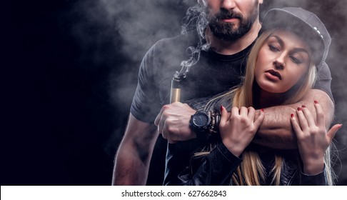 Brutal Man And Sexy Woman Are Vaping. Studio Shooting. Black Background.