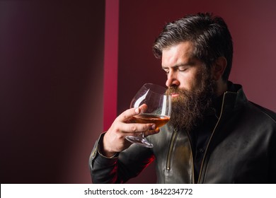 Brutal man tastes whiskey. Whiskey. Brandy. Strong alcohol. Degustation and tasting. Man in leather jacket drinks whiskey. Sommelier degustates whiskey.