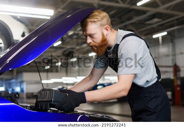A\
brutal man in uniform during technical work with a car at the\
diagnostic station. Replacement of filters and\
liquids