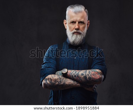 Brutal and mature man with in gangster style poses in dark background with crossed arms.
