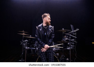 brutal portrait of a man musician with a beard and in black clothes on the background of musical instruments drums