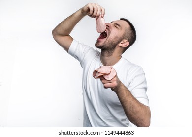 Brutal and real man is eating sliced pieces of meat. He is putting one piece of meat in the mouth and keeping the other pieces in the other hand. Isolated on white background. - Powered by Shutterstock