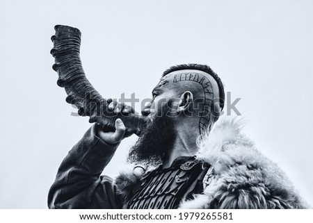 Brutal viking warrior blowing horn outdoors.