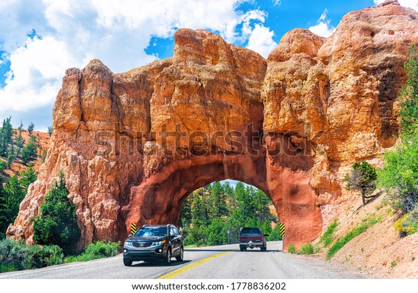 Bryce, USA - August 2, 2019: Road\
highway near Bryce Canyon National park with hole tunnel through\
red orange rock in desert with cars in traffic on summer\
day