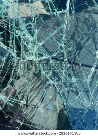 bstract Close Up of Shattered Car Windshield Glass Texture
 Macro detail of cracked and shattered car windshield glass with green tint and spiderweb pattern.