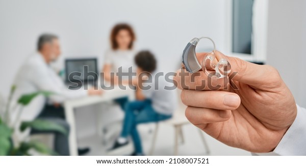 BTE hearing aid in doctor hands, close-up.\
Selection of hearing aids for child patient with audiologist over\
background, soft focus