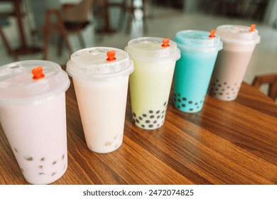 Bubble tea with different flavors in disposable cups with lid on wooden table.