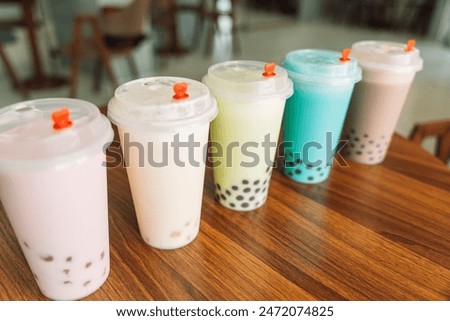 Bubble tea with different flavors in disposable cups with lid on wooden table.