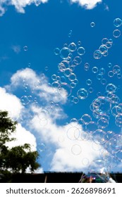 Bubbles float upwards against a bright blue sky with fluffy white clouds. A person's head and shoulder are visible at the top left.