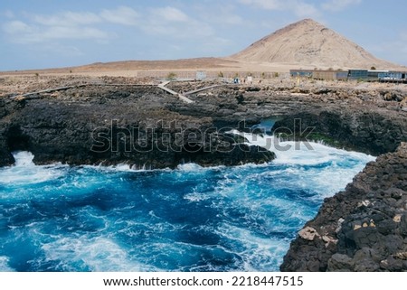 Bubbling bright blue water with white foam in Atlantic ocean against the backdrop of the brown mountain and rocky coast in Buracona blue eye on Sal island in Cape Verde. 
