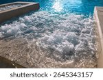 Bubbling section of a pool, where jets or a fountain stir surface into lively ripples and foam. Sunlight glints across water, enhancing the shimmering effect and lending the scene a fresh