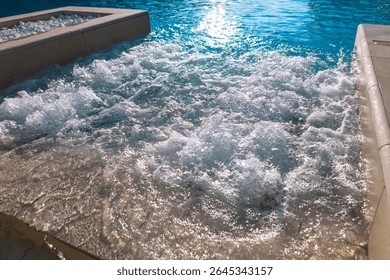Bubbling section of a pool, where jets or a fountain stir surface into lively ripples and foam. Sunlight glints across water, enhancing the shimmering effect and lending the scene a fresh