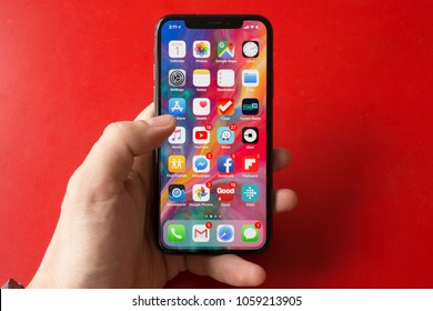 BUCHAREST, ROMANIA - APRIL 1, 2018: Photo Of An Iphone X Home Screen Full Of Icons And Apps On Red Background