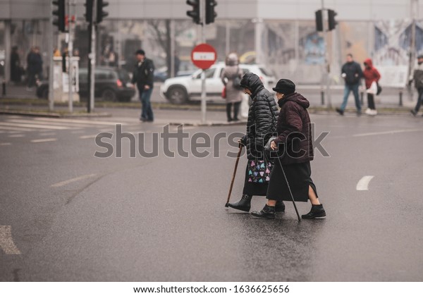 Bucharest, Romania -\
December 20, 2019: Two old women illegally cross the road in the\
middle of a\
crossroad.