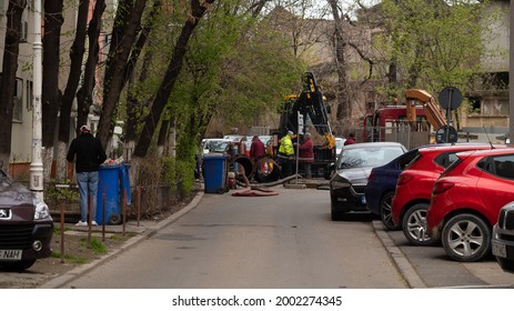 BUCHAREST, ROMANIA - May 15, 2021: Workers Carry Out Repair Work On The City Sewer. Tractor, Repair In The City, Hole In The Asphalt.