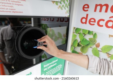 Bucharest, Romania - May 25, 2022: Details with the hands of a man introducing glass bottles in a recycling equipment.