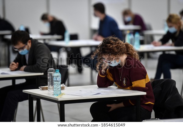 BUCHAREST, ROMANIA -\
NOVEMBER 15, 2020: Large number of students sustaining a written\
exam indoors of a huge hall respecting the social distance measure\
imposed by corona\
virus.