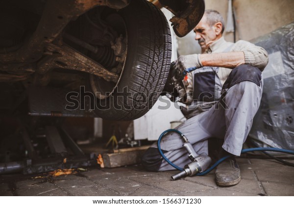 Bucharest,\
Romania - November 21, 2019: Shallow depth of field (selective\
focus) image with a mechanic changing the regular summer tyres of a\
car with winter tyres in a dirty car\
service.