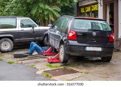 BUCHAREST, ROMANIA - SEPTEMBER 12, 2015: Man Working Under His Wolkswagen Polo Car At A Small Car Service Trying To Fix A Steering System Issue Due To Bad Roads