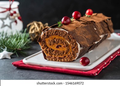 Buche de Noel. Traditional Christmas dessert, Christmas yule log cake with chocolate cream, cranberry. On stone gray background with Christmas tree branches.