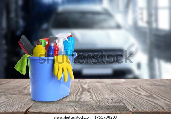 Bucket with cleaning supplies on wooden surface at\
car wash. Space for text