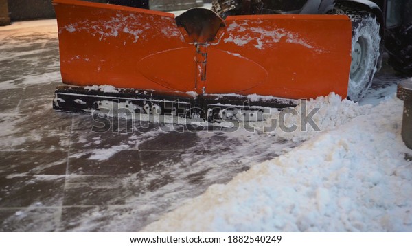 A bucket close-up cleans the sidewalk from snow.\
The tractor cleans the pavement in winter. Tractor cleaning the\
road from the snow. Excavator cleans the streets of large amounts\
of snow in city.