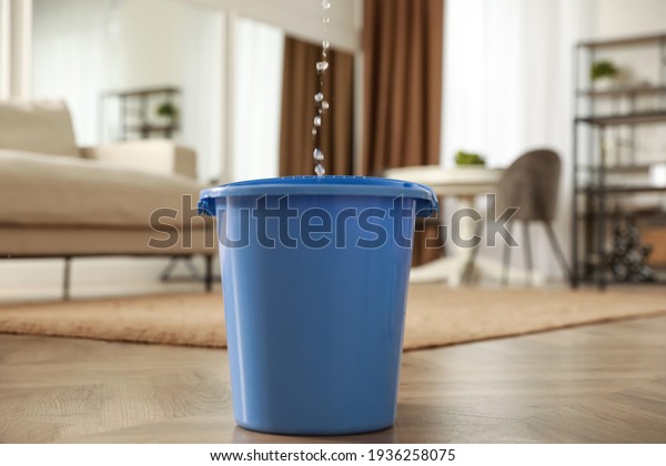 Bucket collecting water from ceiling in living room.\
Leaking roof