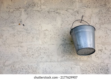 A bucket hangs on a stone wall. Bucket made of galvanized steel hangs on a nail. Empty bucket on the wall.