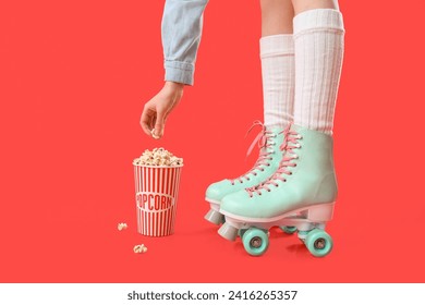 Cubo de palomitas de maíz y piernas de mujer en patines de rodillos sobre fondo rojo