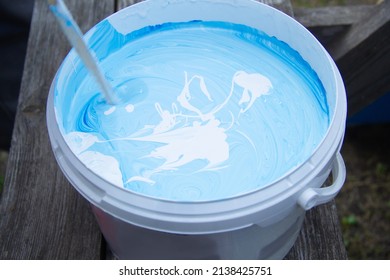 In A Bucket Stir The Blue And White Paint With A Stick