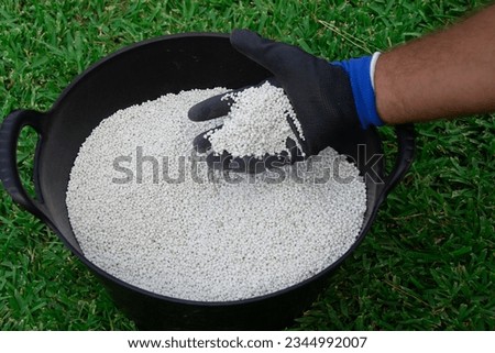 Bucket of white chemical fertilizer in granular format ready to be applied to garden plants. Garden maintenance concept.