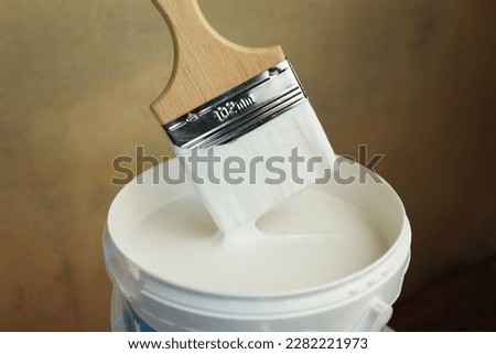 A bucket of white paint and a brush. Painting works in the premises. Tidying up the apartment. Repair of premises. The brush is dipped in white paint