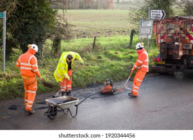 BUCKINGHAM, UK - December 14, 2020. Road Works, Road Crew Team, Men Wearing High Visibility Hi Vis Orange Clothing. Repairing Potholes In A Rural Country Road