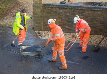 BUCKINGHAM, UK - December 14, 2020. Road Workers Wearing High Visibility Hi Vis Orange Clothing, Repairing Potholes In A Street