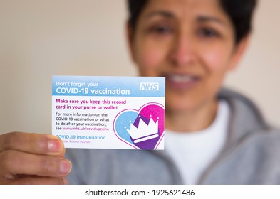 BUCKINGHAM, UK - February 22, 2021. Asian woman holding NHS Covid-19 vaccination record card having received a COVID 19 coronavirus vaccine jab, UK