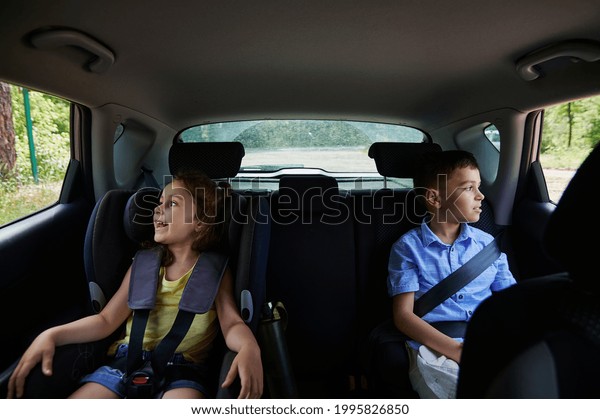 Buckled two children passengers , boy and girl,\
traveling in a safety booster seat inside the car. Safe travel with\
children in the car