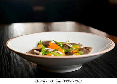 Buckwheat dumplings with fresh mushrooms served on a white plate over black background.