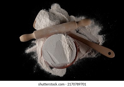 Buckwheat Flour In Clay  With Wooden Spoon And Kitchen Rolling Pin Isolated On Black, Top View