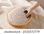 Buckwheat flour in a wooden bowl and raw buckwheat grain on cotton napkin on beige monochrome background. Alternative flour, gluten free flour, healthy nutrition