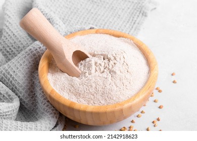 Buckwheat flour in a wooden bowl with wooden scoop and raw green buckwheat grain on light grey concrete background, close up. Alternative flour, gluten free flour, healthy nutrition
