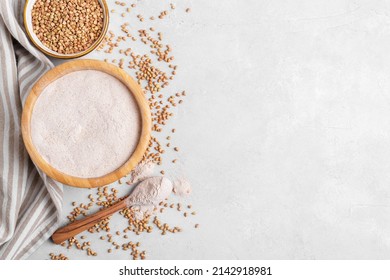 Buckwheat flour in a wooden bowl with wooden spoon and raw green buckwheat grain in a bowl on light grey stone background, close up, top view. Alternative flour, gluten free flour, healthy nutrition
