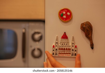 Budapest Fridge Magnet In Hand On Kitchen. Travel To Budapest Concept. Souvenir From Hungary With The Building Of Hungarian Parliament In Miniature. Travel To Europe Memories.