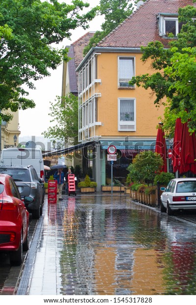 Budapest, Hungary - 04.05.2019: Szentháromság\
street from Matyas-templom, Matthias Church, with house and cars\
reflections on shining wet pavement on a rainy spring day, Buda\
Castle District