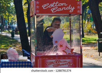 Budapest, Hungary -10-21-2012: A woman making cotton candy in the park. Little girl is watching. Cotton candy is a form of spun sugar.