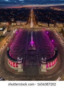 Budapest, Hungary - Aerial drone view of the famous Heroes' Square (Hosok tere) lit up in unique purple and pink color by night with Andrassy street and colorful sunset at background